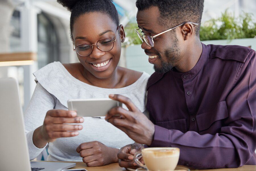 cropped shot deighted happy african couple holds smart phone horizontally watch interesting video have coffee break smile joyfully wears round spectacles 273609 3676