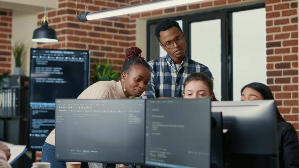 developers brainstorming ideas looking at code on computer screens asking feedback from senior developer
