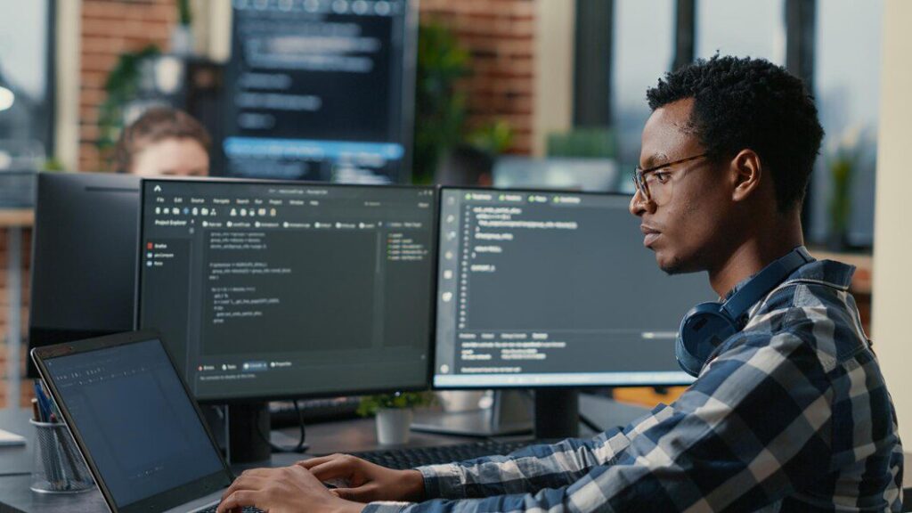 sofware developer thinking while touching beard while typing laptop sitting desk with multiple screens parsing code focused database admin working with team coding background 482257 33556